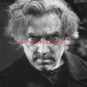 May include: Black and white portrait of a man with a serious expression. He has grey hair and a beard. The photo is from the Hollywoodtreasures.com website.