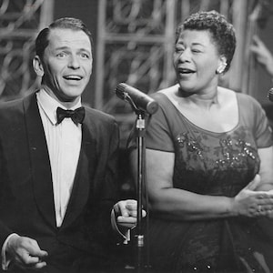 Puede incluir: Una fotografía en blanco y negro de Frank Sinatra y Ella Fitzgerald cantando en micrófonos. Ambos sonríen y parecen estar disfrutando.