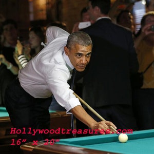 May include: An image of a person playing pool, with a white cue ball and a green felt pool table. The person is wearing a white shirt and black pants. The image is labeled "Hollywoodtreasures.com" and "16" x 20".
