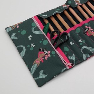 Könnte beinhalten: Eine grüne Reißverschlusstasche mit einem Meerjungfrauen- und Blasenmuster. Die Tasche ist geöffnet und zeigt ein Set aus Holzstricknadeln und eine Schere.