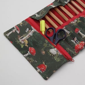 May include: A green zippered pencil case with a whimsical fairy and mushroom print. The case is open, revealing a red interior with slots for pencils and a zippered pocket. A yellow highlighter and a pair of scissors are in the pocket.