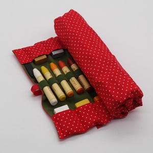 May include: Red fabric roll-up case with white polka dots, containing a set of colored crayons and a white eraser. The case has green fabric lining with individual slots for each crayon and eraser.