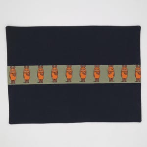 May include: A rectangular, navy blue fabric item with a horizontal band of cartoon mice. The mice are orange with brown ears and feet, standing on a light green background. The item appears to be a decorative piece or accessory.