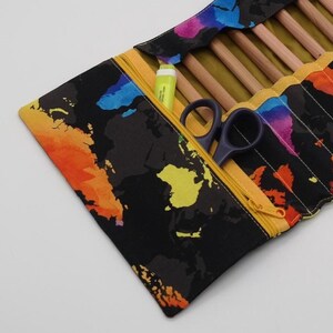 May include: A black pencil case featuring a vibrant world map pattern. The case has a yellow zip and holds pencils, a highlighter, and small scissors. The case is open, displaying its contents.