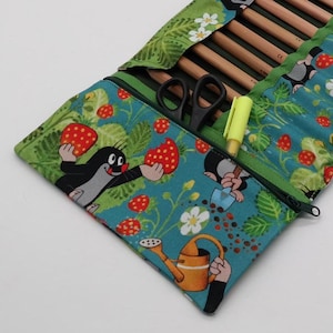 Könnte beinhalten: Türkisfarbenes Federmäppchen mit einem skurrilen Erdbeer- und Cartoon-Maulwurf-Print. Das Etui ist geöffnet und zeigt Bleistifte, eine Schere und einen gelben Textmarker. Es hat einen grünen Reißverschluss und Besatz.