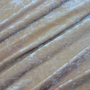 May include: Close-up of a folded, textured fabric in shades of gold and tan. The fabric has a crushed velvet appearance with subtle variations in color and highlights. The folds create diagonal lines across the frame.