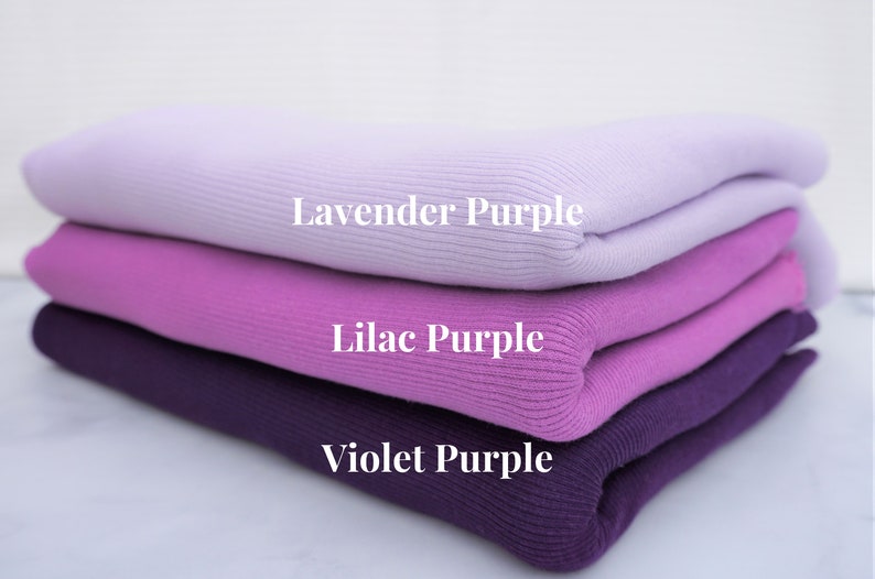May include: A stack of folded knitwear in shades of purple: lavender, lilac, and violet. The image displays the color names on each layer. The fabric has a ribbed texture.