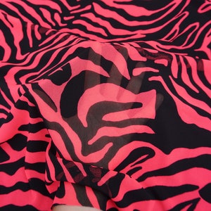 May include: Close-up of a sheer fabric with a bold zebra stripe pattern. The fabric features vibrant neon pink stripes against a black background. The material appears lightweight and flowing, suitable for apparel or decorative projects.