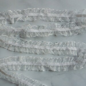 May include: White ruffled lace trim with an elastic band. The delicate, sheer fabric is gathered to create a ruffled edge. This trim is suitable for sewing, crafting, and adding a decorative touch to garments or accessories.