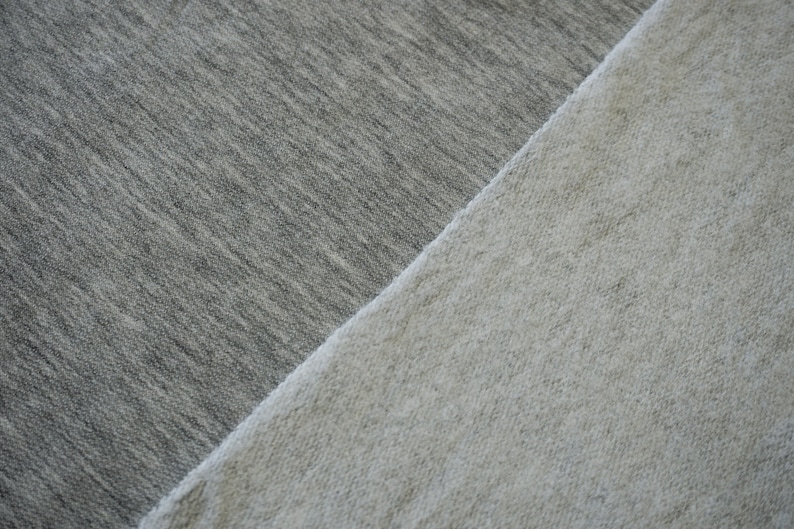 May include: Close-up of two sections of fabric. One section is a medium gray color, and the other is a light beige color. The fabrics are angled against each other, creating a diagonal line. The textures appear soft and possibly knitted.