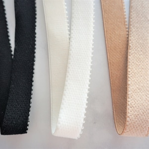 May include: Close-up of four different elastic bands. The bands are black, off-white, white, and tan. The black and white bands have a textured, dotted edge. The tan band is smooth. The off-white band is ribbed.