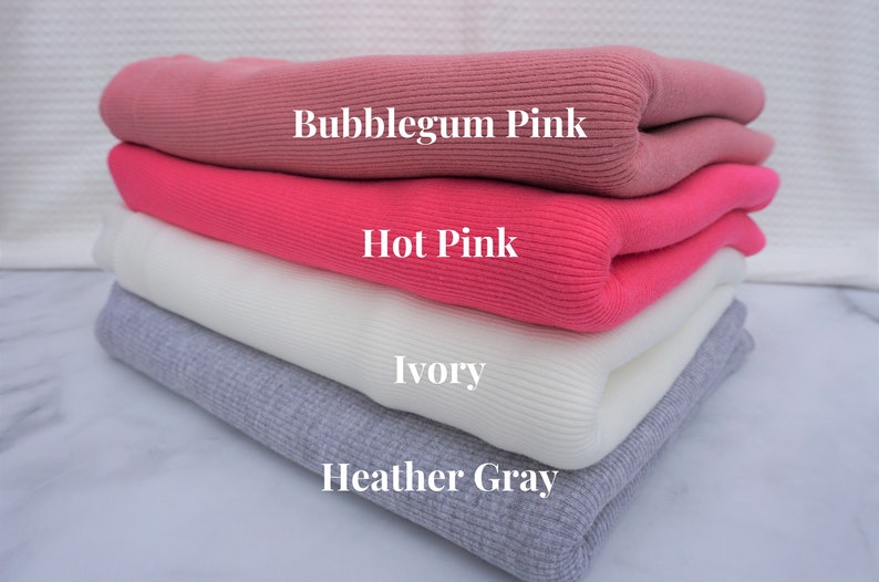 May include: A stack of folded ribbed knit fabric in shades of pink, ivory, and gray. The colors are labeled "Bubblegum Pink", "Hot Pink", "Ivory", and "Heather Gray". The fabric has a soft, textured appearance.
