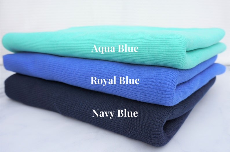 May include: Three folded knit fabrics in shades of blue: aqua, royal, and navy. The aqua blue fabric is at the top, followed by royal blue, and navy blue at the bottom. The names of the colors are written on the fabric.