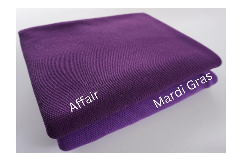 May include: Two folded purple fabrics, one a darker shade than the other. The top fabric is labeled "Affair" and the bottom fabric is labeled "Mardi Gras" in white text. The fabrics appear to be made of a ribbed material.