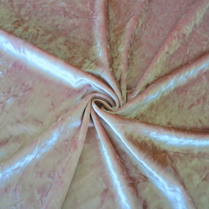 May include: A close-up shot of a light pink velvet fabric with a swirling pattern. The fabric has a soft, textured appearance with subtle variations in color and highlights. The folds and creases create a dynamic, flowing effect.