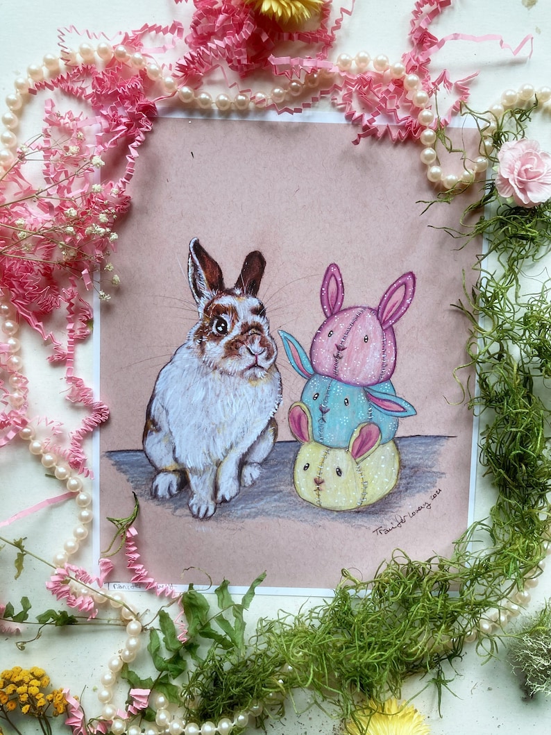 May include: A white and brown rabbit sits next to a stack of three plush toys. The toys are pink, blue, and yellow with embroidered faces. The image is signed "Tangle Loving 2014".