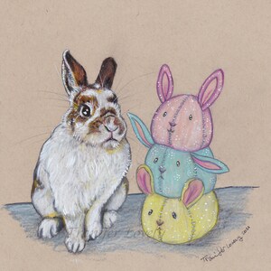 May include: A white and brown rabbit sits next to a stack of three handmade fabric bunny toys. The toys are pink, blue, and yellow with white stitching. The toys are stacked on top of each other.