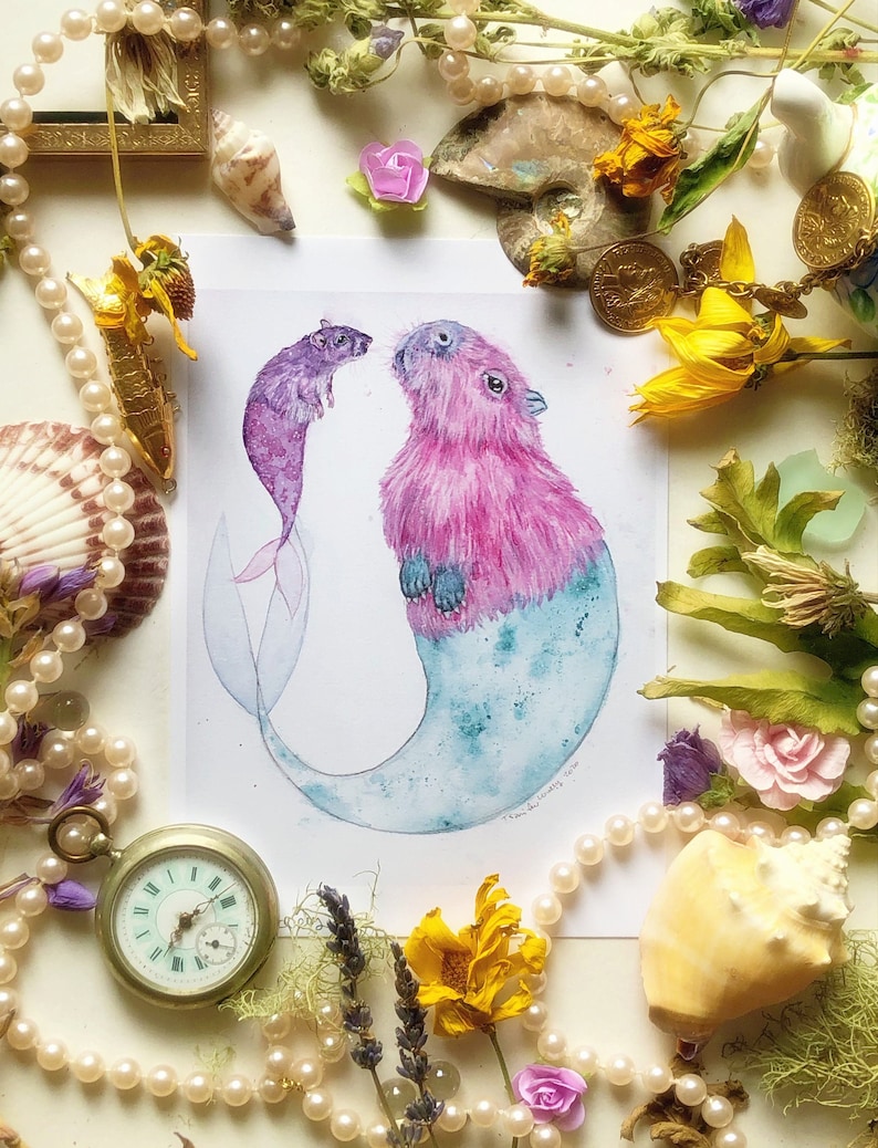 May include: Watercolor painting of a pink capybara mermaid with a blue tail and a purple rat mermaid with a blue tail. The painting is on a white background.