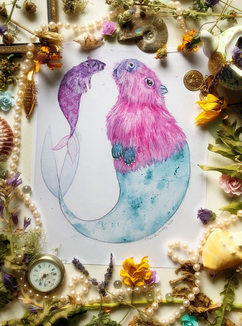 May include: Watercolor painting of a pink and blue capybara mermaid and a purple rat mermaid. The capybara mermaid is looking up at the rat mermaid. The painting is surrounded by pearls, flowers, and other decorative items.