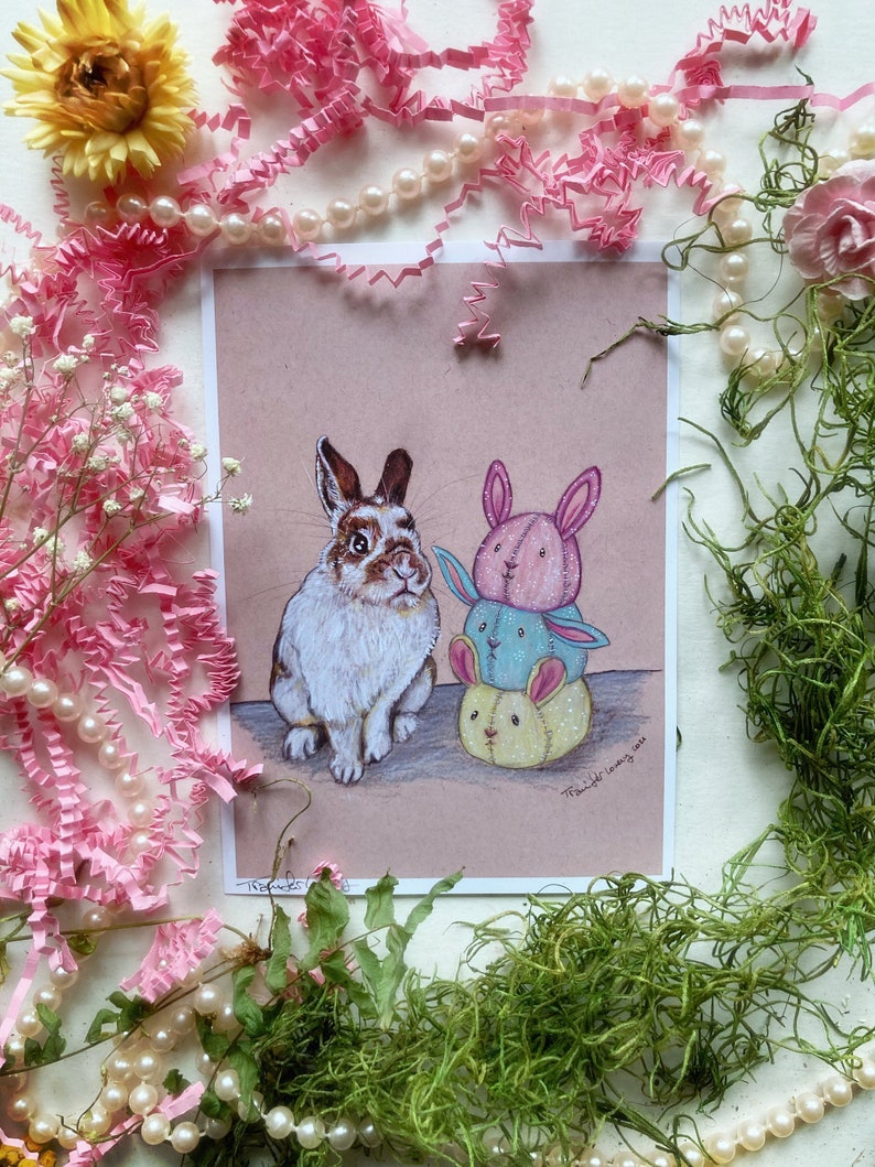 May include: A hand-drawn illustration of a brown and white rabbit sitting next to a stack of three colorful bunny plushies. The plushies are pink, blue, and yellow. The illustration is on a pink background and has the artist's signature and date in the bottom right corner.