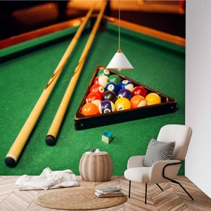 May include: A green felt pool table with two wooden cues and a rack of billiard balls in a triangle formation. The balls are numbered and colored red, yellow, blue, and green.