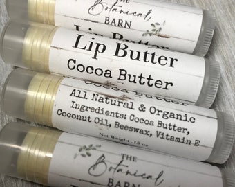 May include: Four lip butter tubes from The Botanical Barn, labeled "Lip Butter Cocoa Butter." The tubes have white labels with black text and a botanical design. Ingredients include cocoa butter, coconut oil, beeswax, and vitamin E. Net weight is .15 oz.