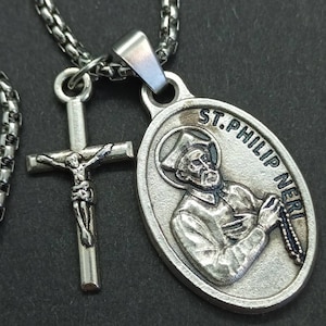 Peut inclure: Collier pendentif religieux argenté avec deux breloques. L'une est un pendentif ovale avec le texte "ST. PHILIP NERI" et une image détaillée. L'autre est un crucifix. La chaîne du collier est également argentée.