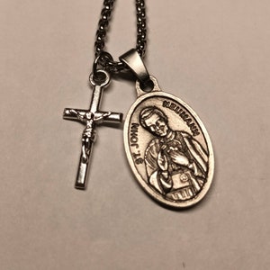 May include: Silver chain necklace with a silver cross and a silver oval pendant featuring a religious figure. The pendant has the text "St. John Neumann" on it.