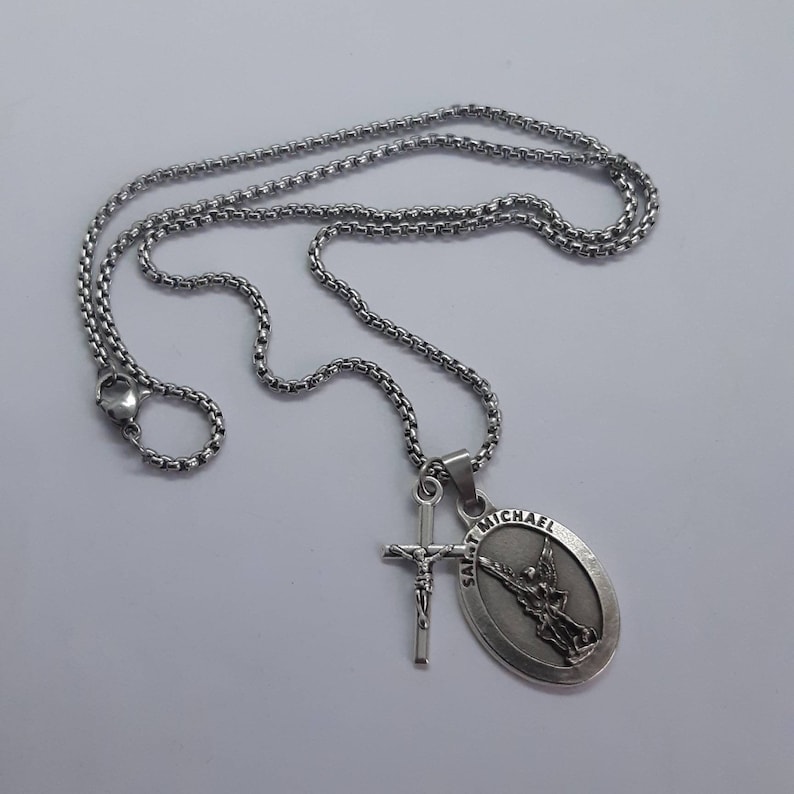 K&ouml;nnte beinhalten: Eine silberfarbene Halskette mit einer Kette und zwei Anh&auml;ngern. Ein Anh&auml;nger ist ein Kreuz mit einer Jesusfigur, der andere ein ovaler Anh&auml;nger mit den Worten "SAINT MICHAEL" und einem Engelbild.