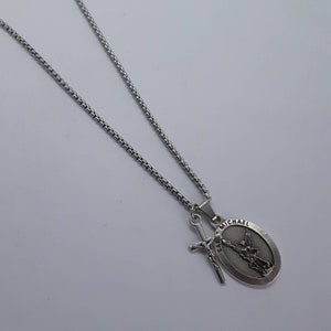 K&ouml;nnte beinhalten: Silberfarbene Halskette mit einem Anh&auml;nger mit einem ovalen Saint Michael Medaillon und einem Schwert-Charm. Die Kette hat ein Box-Link-Design. Der Anh&auml;nger zeigt Saint Michael mit dem Text "SAINT MICHAEL".