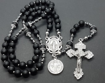 Op de afbeelding: Een zwarte onyx rozenkrans met zilveren kralen en een zilveren kruisbeeld en medaillons. De medaillons tonen afbeeldingen van de Maagd Maria en Sint Benedictus.
