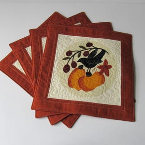 May include: Set of six orange and cream quilted placemats featuring a black bird and pumpkins design.