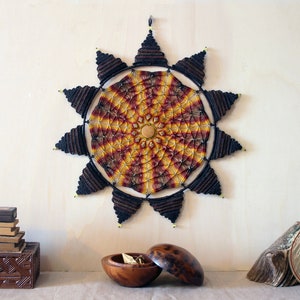 May include: A large, circular macrame wall hanging with a sunburst design in shades of red, yellow, and brown. The macrame is made with thick cord and has a beaded border.