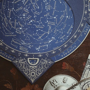 May include: A detailed celestial chart with constellations, zodiac signs, and star names, printed on dark blue paper. The chart features intricate designs and a circular scale, with the text "FEBRUARY" and "NOVEMBER" visible. The chart is set on a dark wooden surface.