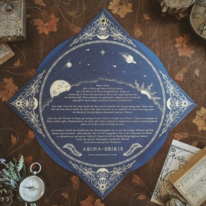 May include: A dark blue, star-themed card with ornate gold detailing, featuring celestial illustrations of the moon, sun, and stars. The card includes text in multiple languages and is surrounded by other vintage-style items, including a compass and a small wooden box.