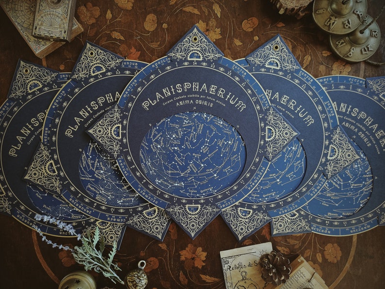May include: A collection of dark blue Planisphaerium celestial charts with gold accents. Each chart features a detailed star map and the title "Planisphaerium" in elegant lettering. The charts are arranged on a wooden surface, evoking a vintage aesthetic.