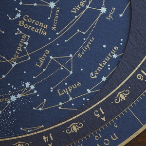 May include: Close-up of a dark blue celestial chart with gold lettering and star patterns. Constellations like Libra, Scorpius, and Hercules are labeled. A circular scale with numbers and months is visible.