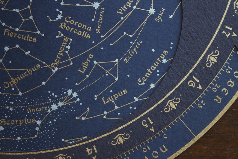 May include: Close-up of a dark blue celestial chart with gold lettering and star patterns. Constellations like Libra, Scorpius, and Hercules are labeled. A circular scale with numbers and months is visible.