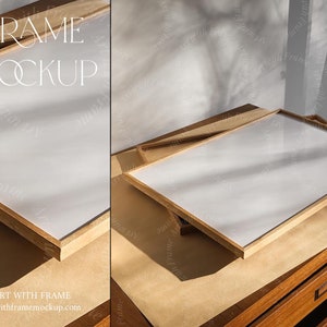 May include: A wooden frame mockup with a white surface, resting on a wooden table. The text "FRAME MOCKUP" is displayed at the top, with "ART WITH FRAME" and a website address at the bottom. The scene is lit with natural light.