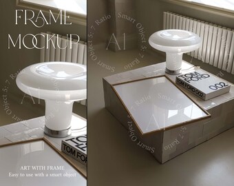 May include: A white ceramic table lamp with a mushroom-shaped shade sits on a white tiled surface. A framed picture sits on the surface next to the lamp. The frame is made of natural wood and has a white mat. The picture is blank. The lamp is labeled "TOM FORD 002".