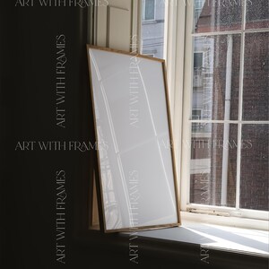 May include: A wooden frame with a white mat and a white background. The frame is leaning against a window with a view of a building and a rainy sky.