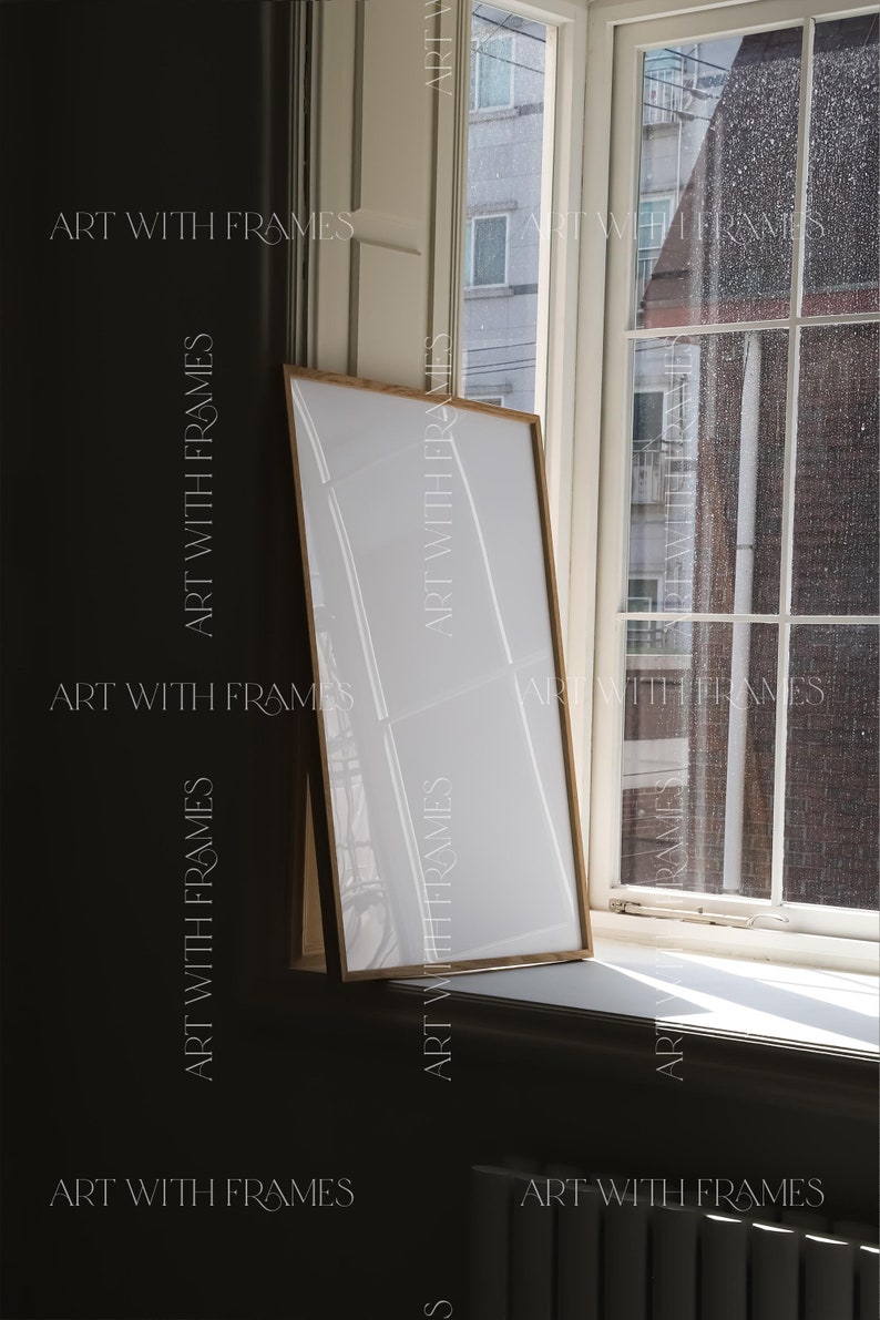 May include: A wooden frame with a white mat and a white background. The frame is leaning against a window with a view of a building and a rainy sky.