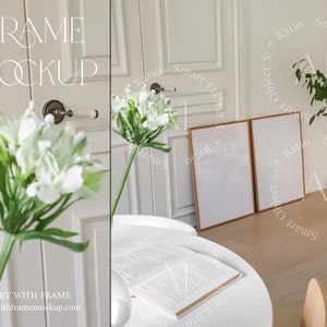 May include: Two empty, light wood framed pictures with white mats hanging on a white wall. The frames are side by side and are in a modern living room setting.