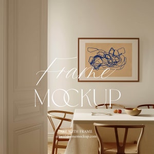 Könnte beinhalten: Ein brauner Holzrahmen mit einem beigefarbenen Passepartout und einer blauen abstrakten Zeichnung an einer hellbeigen Wand in einem Esszimmer mit einem weißen Tisch und zwei Holzstühlen.