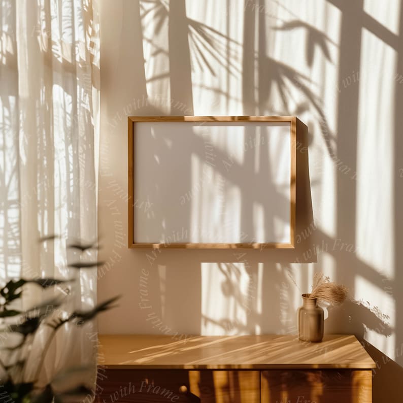 K&ouml;nnte beinhalten: Ein Holzrahmen mit einem wei&szlig;en Passepartout und einem wei&szlig;en Hintergrund h&auml;ngt an einer hellbraunen Wand. Die Wand wird von den Schatten eines Fensters mit wei&szlig;en Vorh&auml;ngen beleuchtet. Eine Vase mit getrockneten Blumen steht auf einem Holztisch.