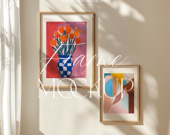 May include: Two framed art prints on a white wall. The print on the left features a vase of orange tulips on a pink background. The print on the right features abstract shapes in blue, yellow, pink, and brown.