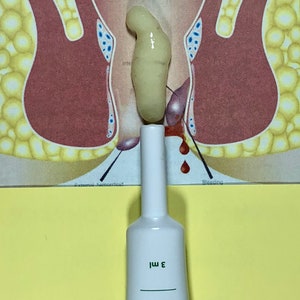 May include: A white tube of hemorrhoidal cream with green text that reads "Benefitelium Hemorrhoidal Cream 3 ml". The tube is sitting on a yellow surface in front of a medical illustration of the rectum.