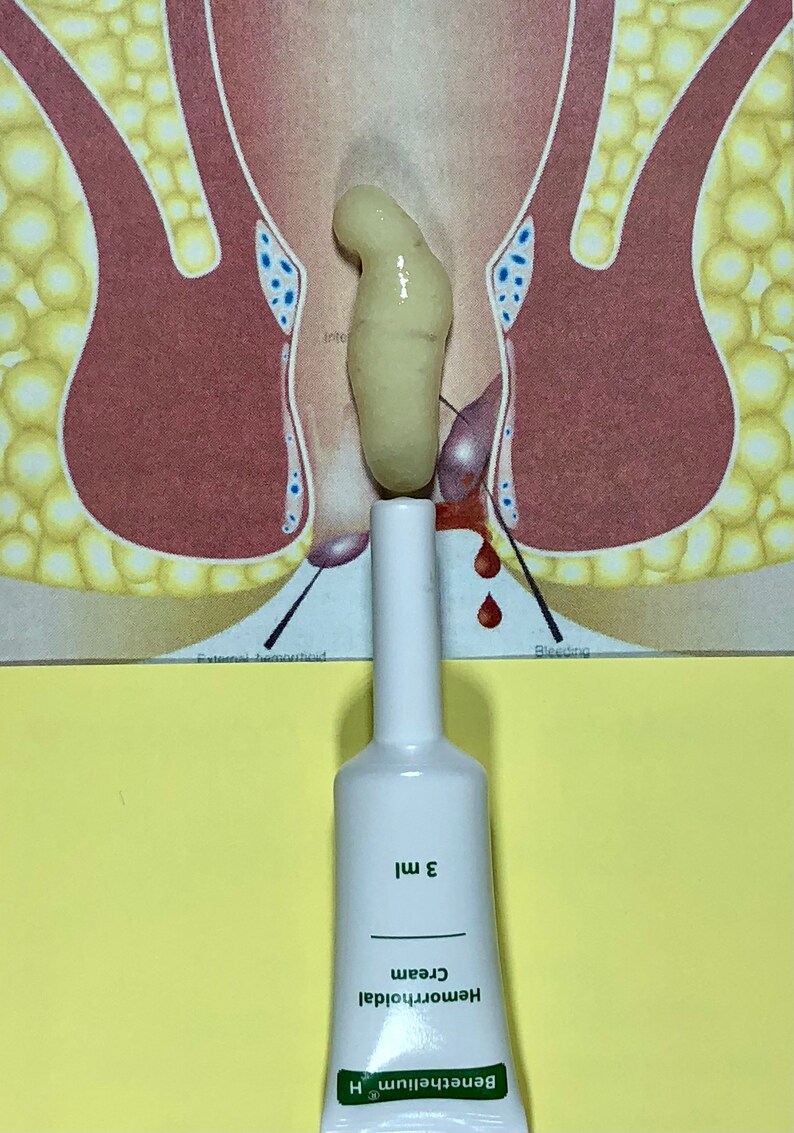 May include: A white tube of hemorrhoidal cream with green text that reads "Benefitelium Hemorrhoidal Cream 3 ml". The tube is sitting on a yellow surface in front of a medical illustration of the rectum.