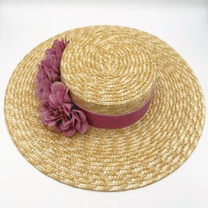 Puede incluir: Un sombrero de paja de ala ancha con una cinta rosa y un adorno de flores rosas.