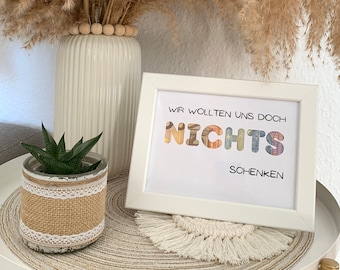 Peut inclure: Une impression encadrée blanche avec le texte "Wir wollten uns doch nichts schenken" en lettres colorées. Les lettres sont faites de papier à motifs. L'impression est posée sur une table avec une petite plante succulente en pot et un pompon blanc.